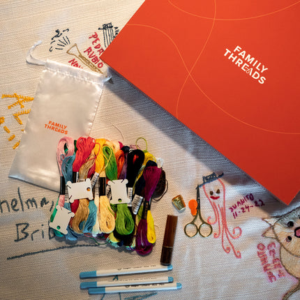 Family Threads tablecloth with markers, threads, and the keepsake box arranged on an embroidered family tablecloth.
