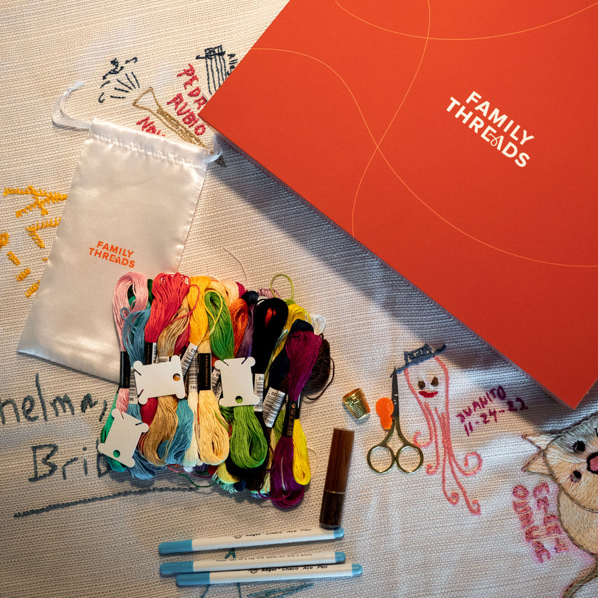 Family Threads tablecloth with markers, threads, and the keepsake box arranged on an embroidered family tablecloth.