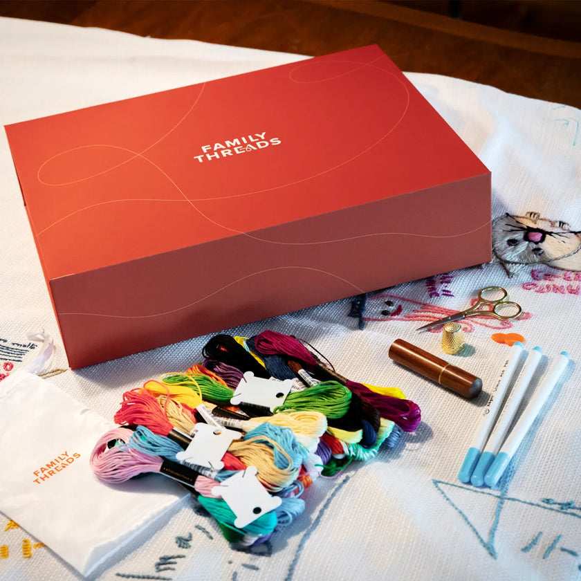 Family Threads keepsake box with embroidery kit, threads, and scissors on tablecloth.