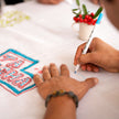 Family member signing the tablecloth during a holiday gathering before the names are embroidered.