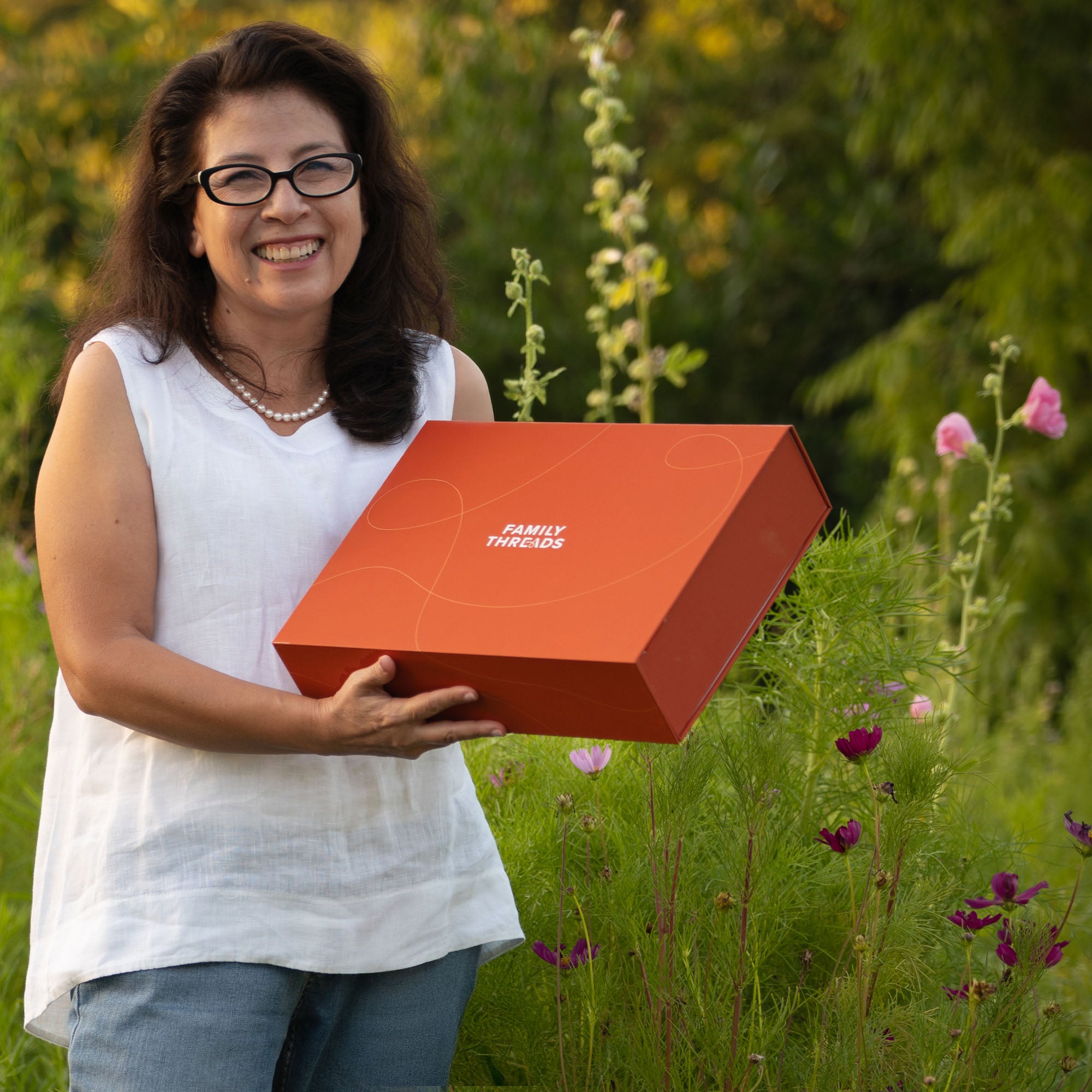 Thelma, founder of Family Threads, holding the signature orange keepsake box outdoors.